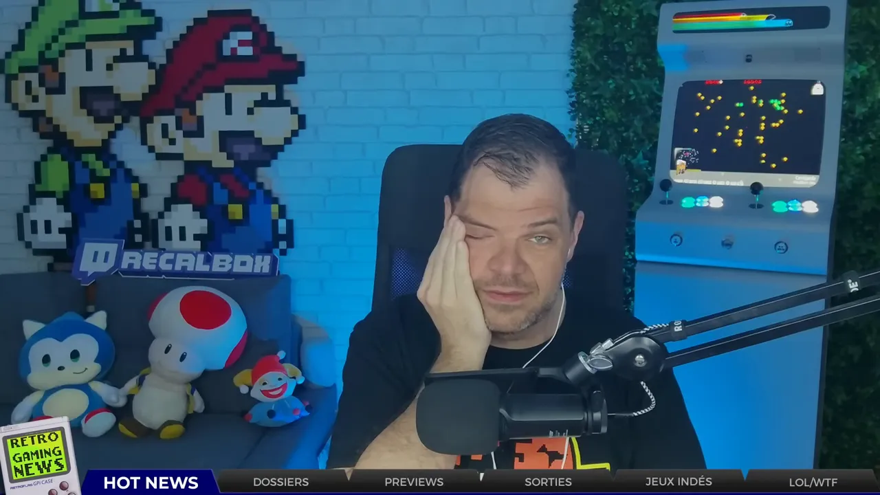 Animateur en studio rétro, main sur la joue, air exaspéré ; borne d'arcade et peluches rétro en arrière-plan