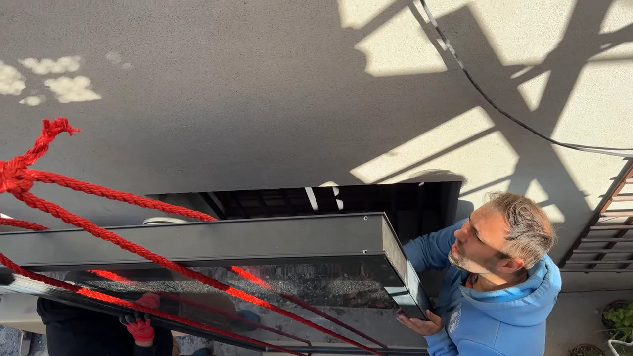 Installateur positionnant un panneau aérothermique depuis l'extérieur avec des cordes rouges