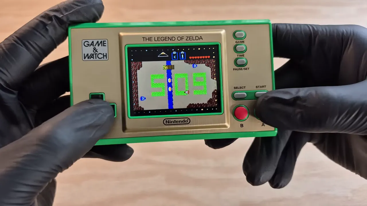 Zelda Game & Watch avec écran affichant une interface de jeu, tenue par des gants noirs