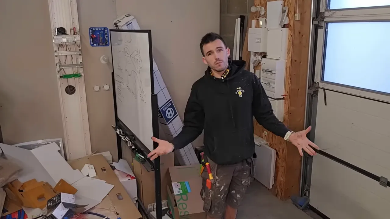 Présentateur dans son atelier face à la caméra, outils et tableau électrique en arrière-plan