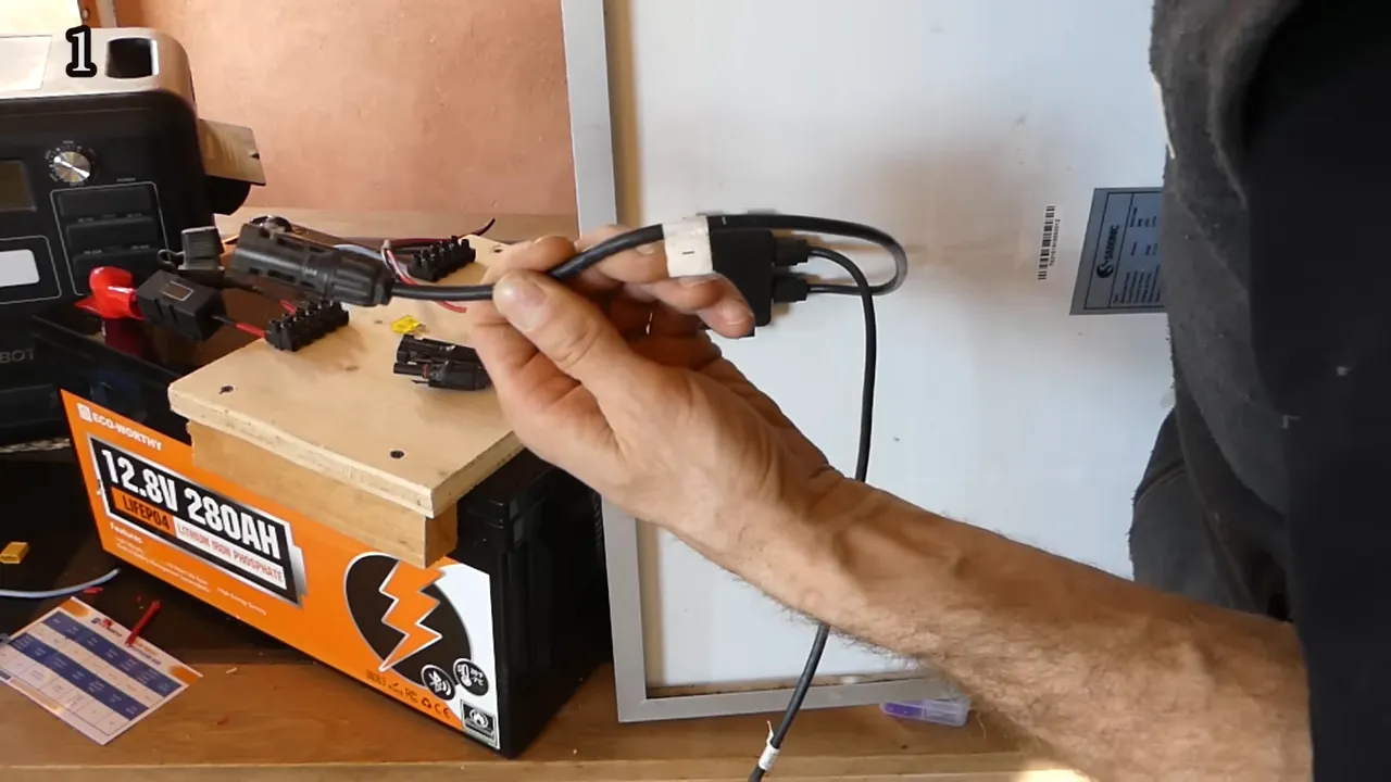 Main tenant un câble de connexion DC devant une batterie ECO-WORTHY 12.8V 280Ah avec la station en arrière-plan