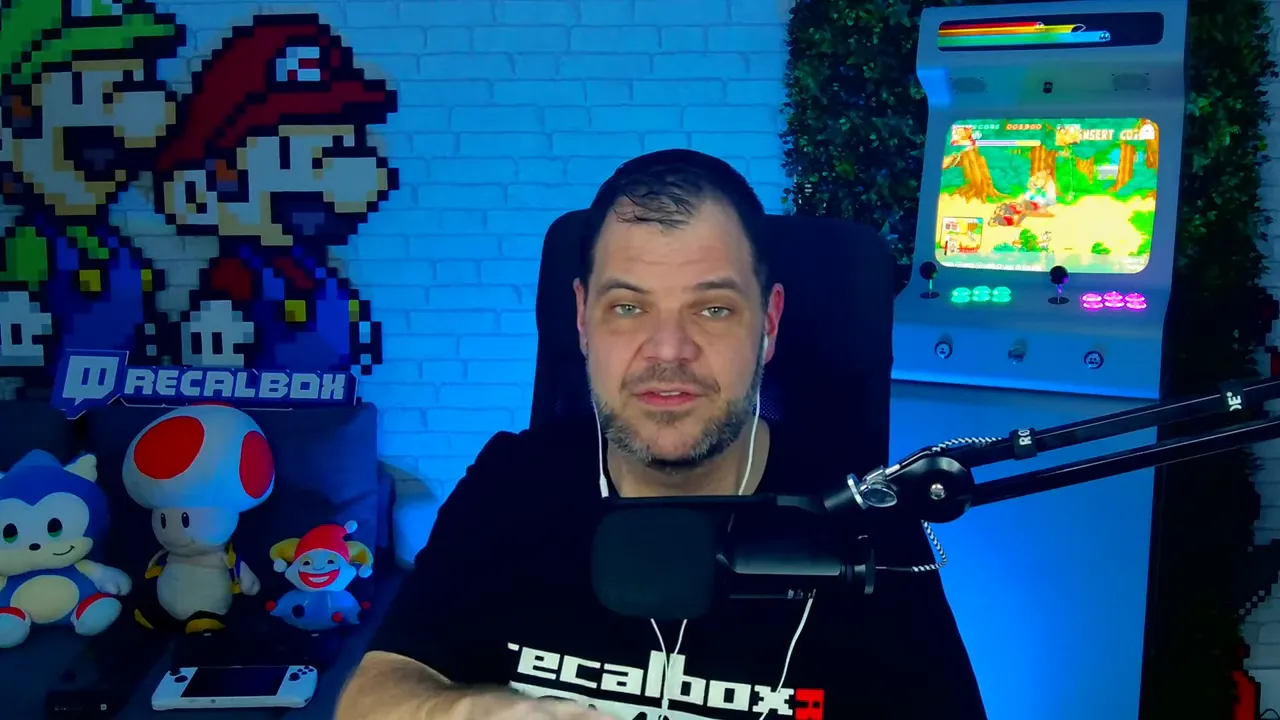Plan studio net montrant l'animateur face caméra, pixel art Mario et une borne d'arcade en arrière‑plan