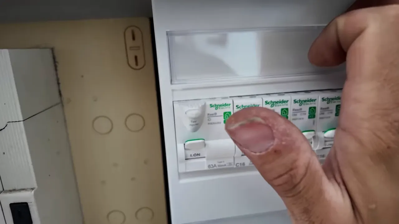 Main vérifiant un disjoncteur modulaire Schneider dans un tableau électrique