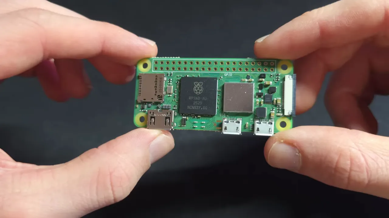 Raspberry Pi Zero 2 W tenu entre deux doigts, vue de dessus montrant la puce et les ports micro‑USB.