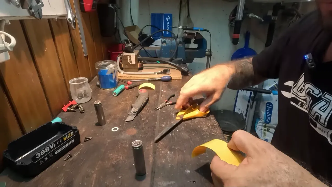 Mains découpant de la gaine isolante jaune près de cellules 18650 prêtes à être isolées