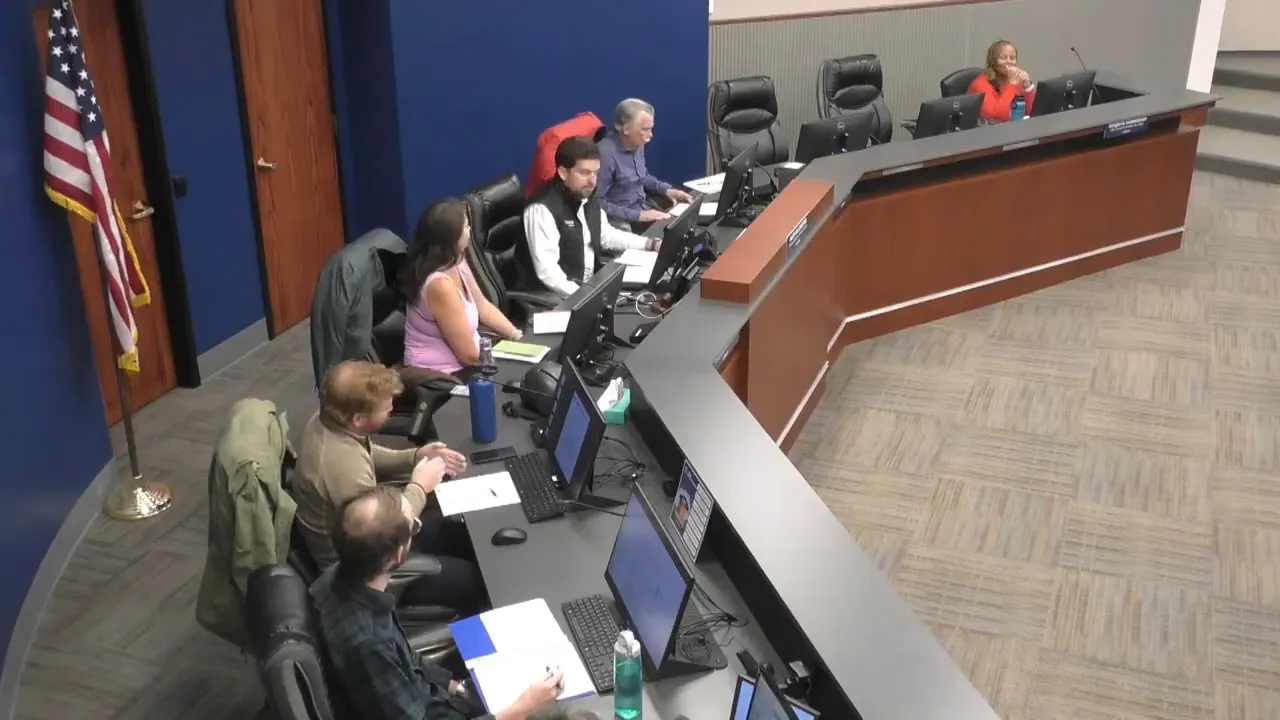 High-clarity wide shot of an advisory board meeting showing members seated at a curved dais with monitors and the public seating area visible.