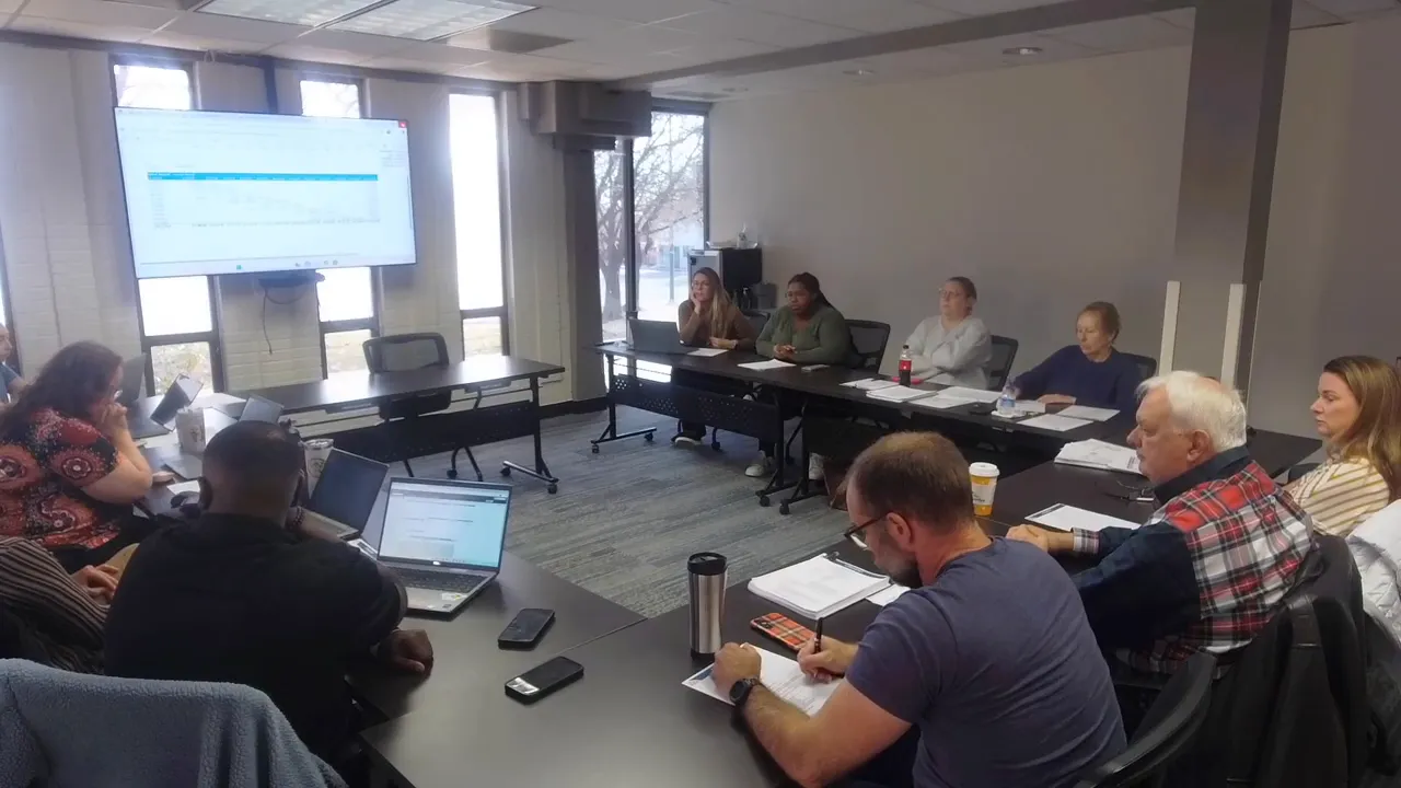 Wide conference-room image showing Longmont Housing Authority board members and staff seated around a table with a presentation screen visible as they follow the agenda.