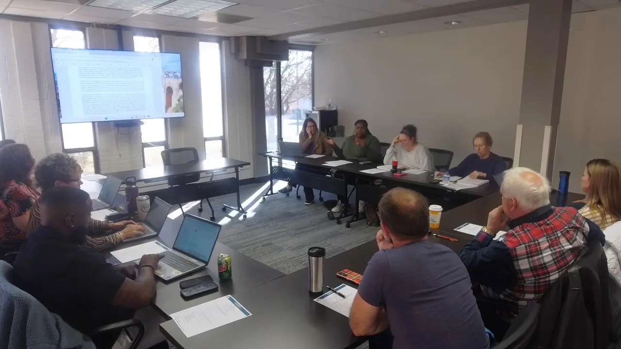 Conference room shot of the Longmont Housing Authority meeting with two panelists gesturing while others listen and take notes.