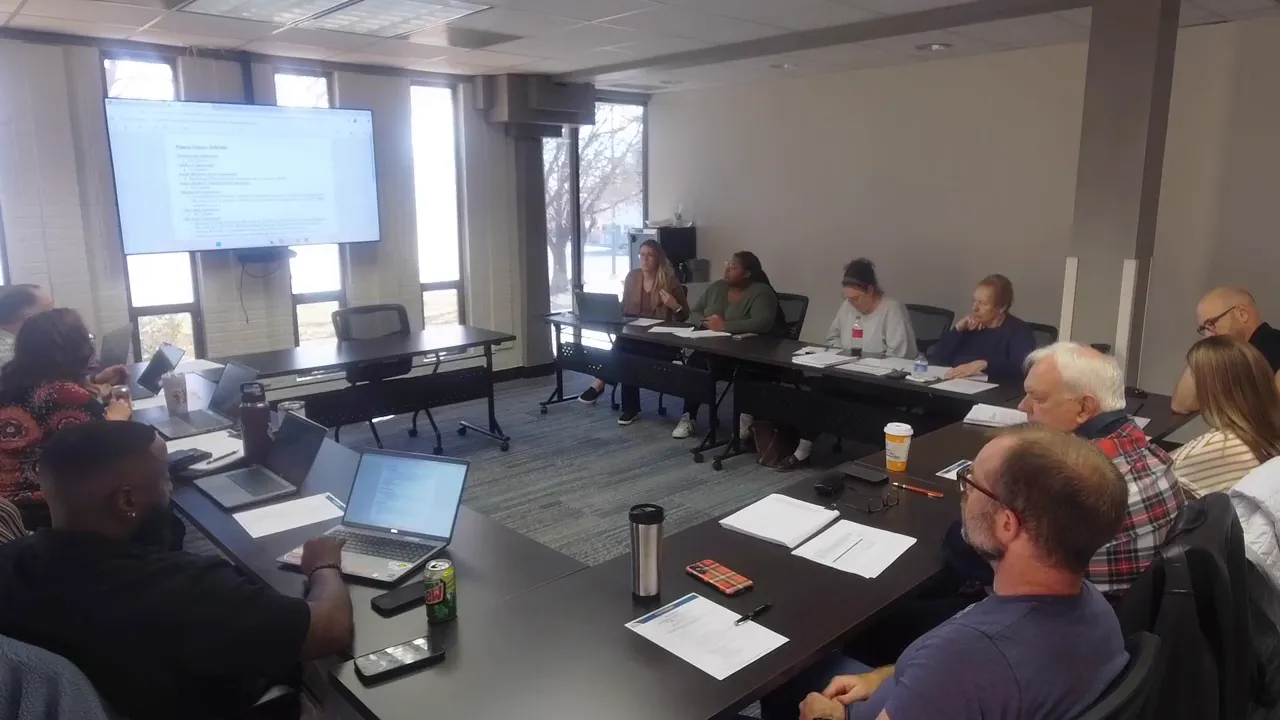 Conference room shot of the Longmont Housing Authority board meeting with visible documents, laptops and a presentation screen.