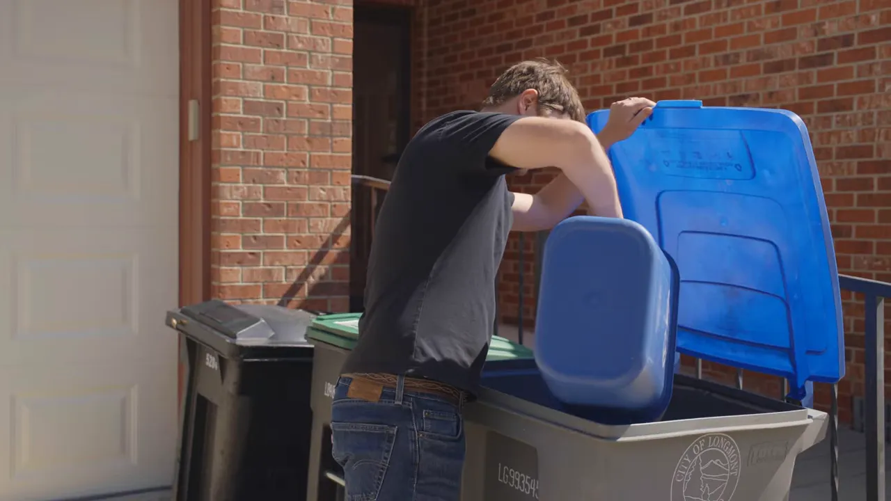 Where Does My Recycling Go? A Longmont Guide to Recycling Right 12 Resident placing a small blue recycling bin into a larger curbside cart with the City of Longmont logo visible