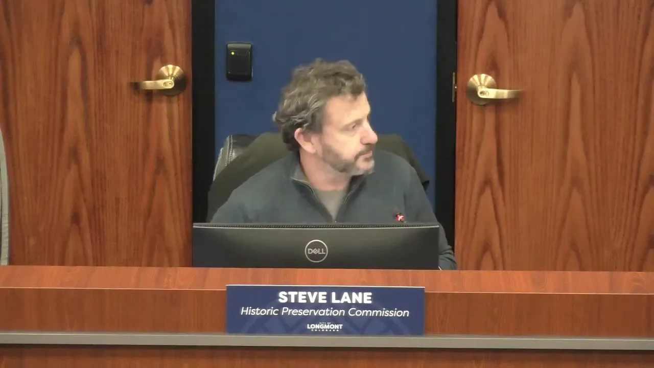 Frontal view of a commission member seated at the dais behind a computer monitor with a visible nameplate on the bench.