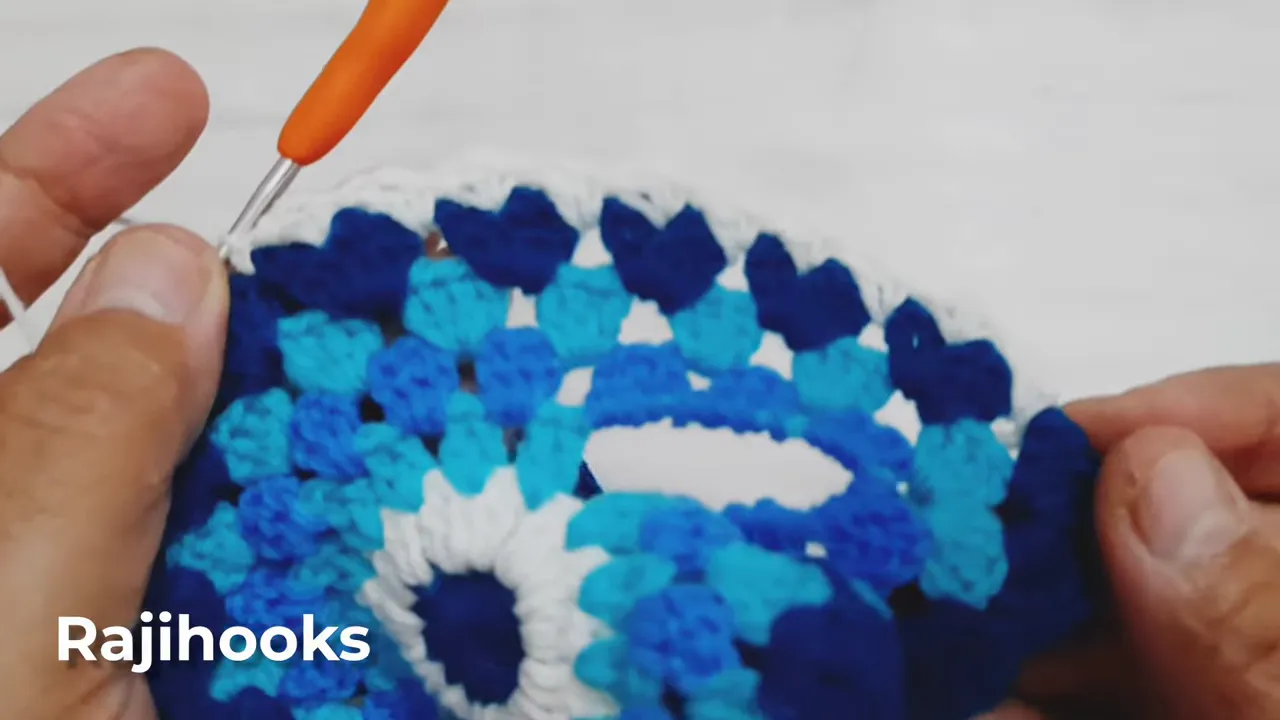 Hands holding a blue crochet motif with small white points along its dark blue outer border