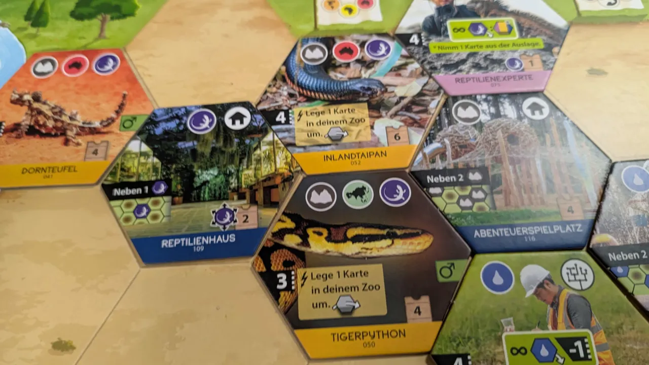 Nahaufnahme von Artengarten Hex‑Plättchen mit Tigerpython, Reptilienhaus und Gehege‑Symbolen