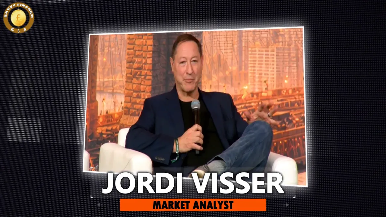 Market-analyst guest seated in a framed studio overlay, holding a microphone and speaking to camera