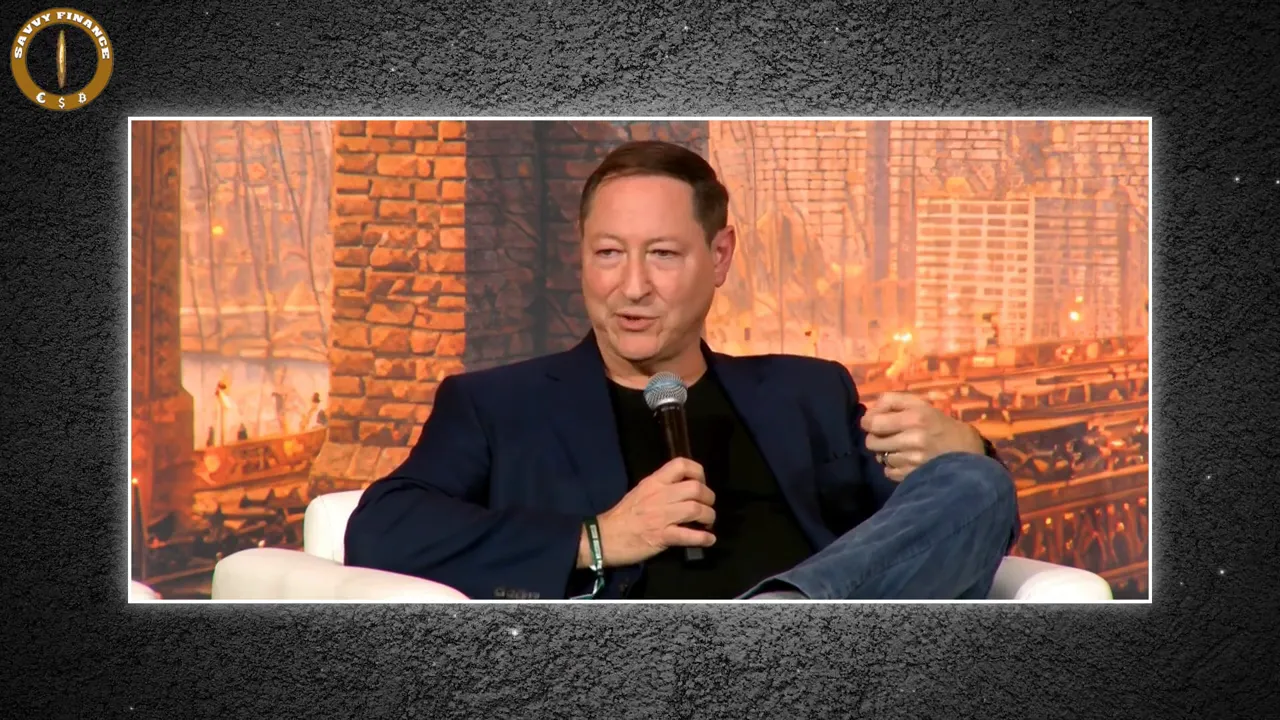 Conference panelist gesturing while holding a microphone in front of a warm, textured stage backdrop