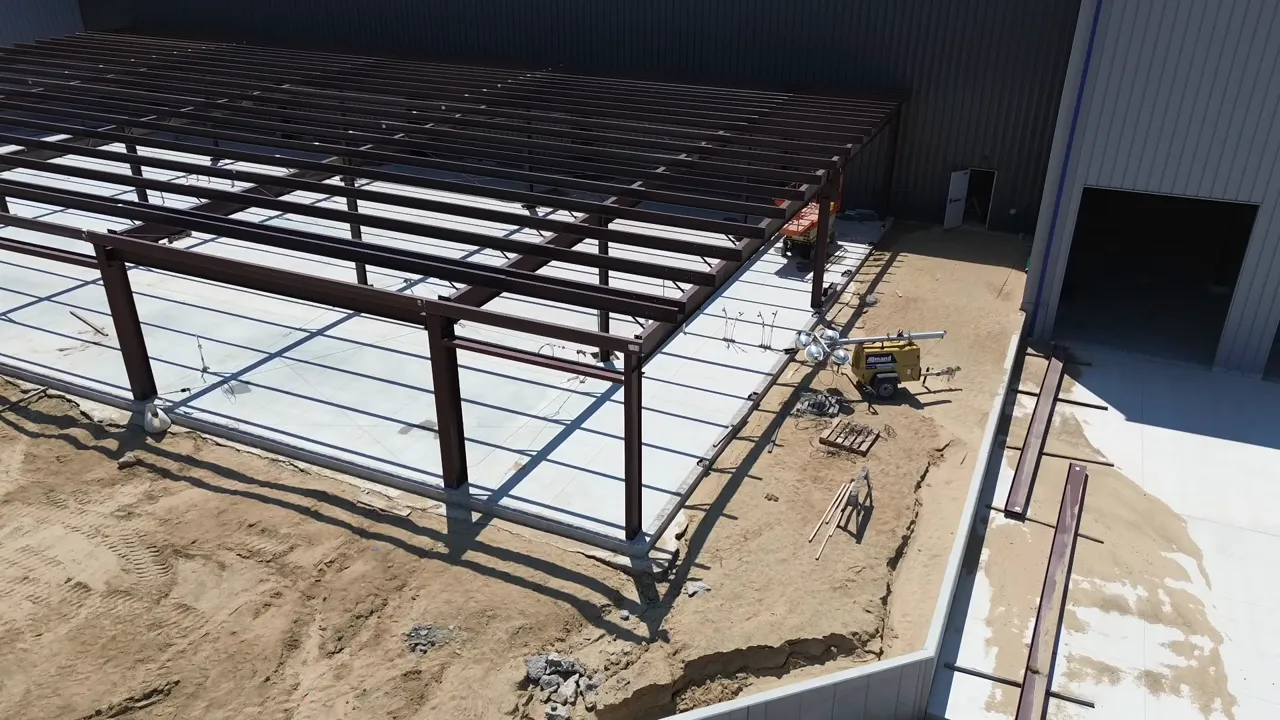 Wide aerial shot of a steel-frame commercial building, concrete slab, and adjacent site equipment