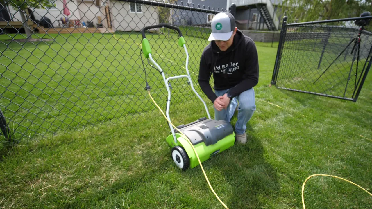 Electric dethatcher operating on a lawn as a person guides it in a fenced yard