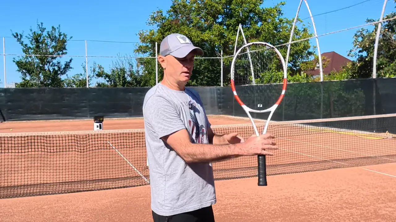 Coach holding a tennis racquet upright with forearm and racquet forming a right angle