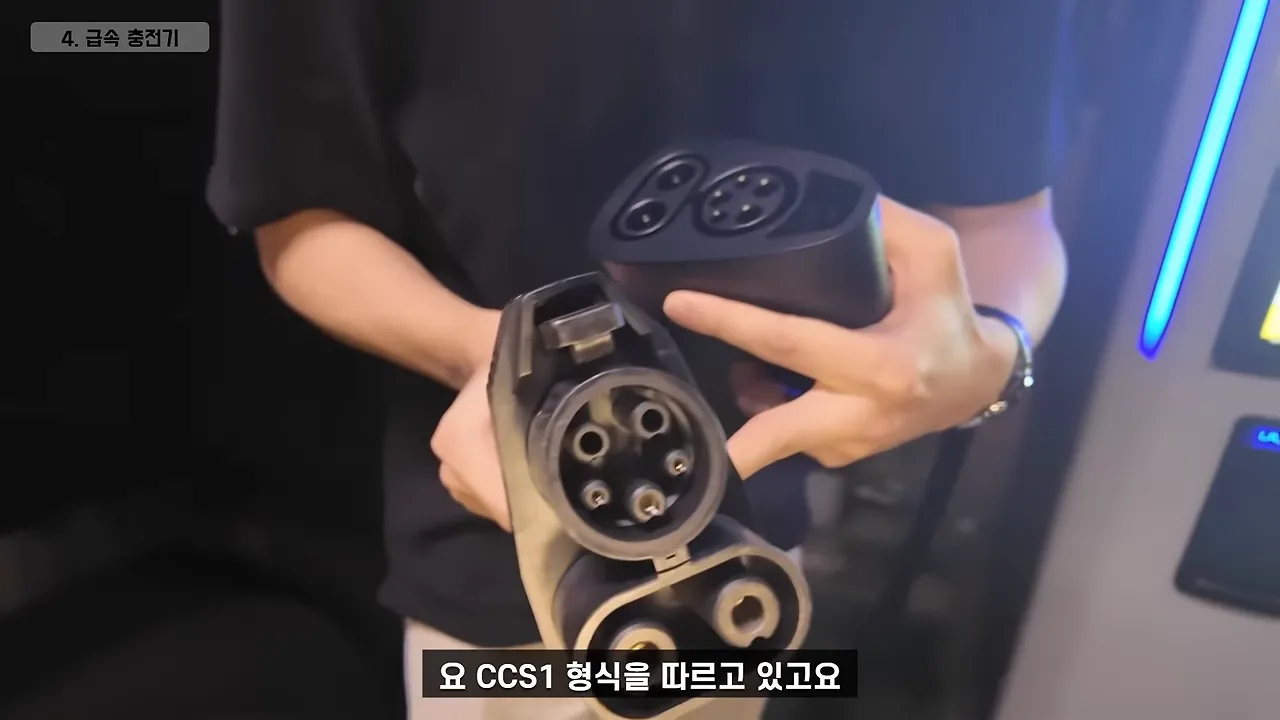 급속 충전기 앞에서 CCS1 커넥터와 테슬라용 어댑터를 들고 있는 모습