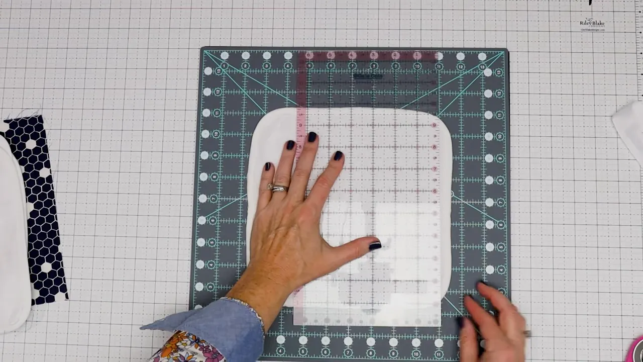 Quilting ruler placed over a white washcloth square on a cutting mat to measure a 4-inch square before cutting.