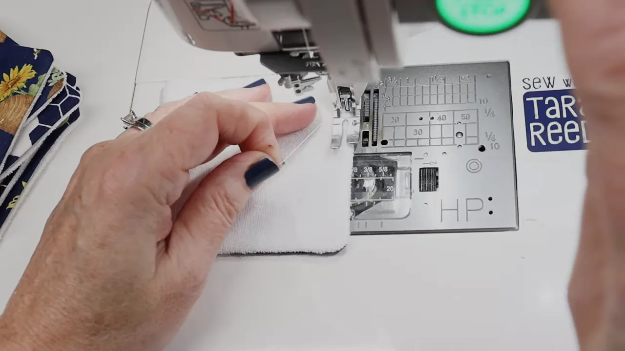 Hand pulling up the bobbin thread with a fabric pad positioned under the sewing machine needle