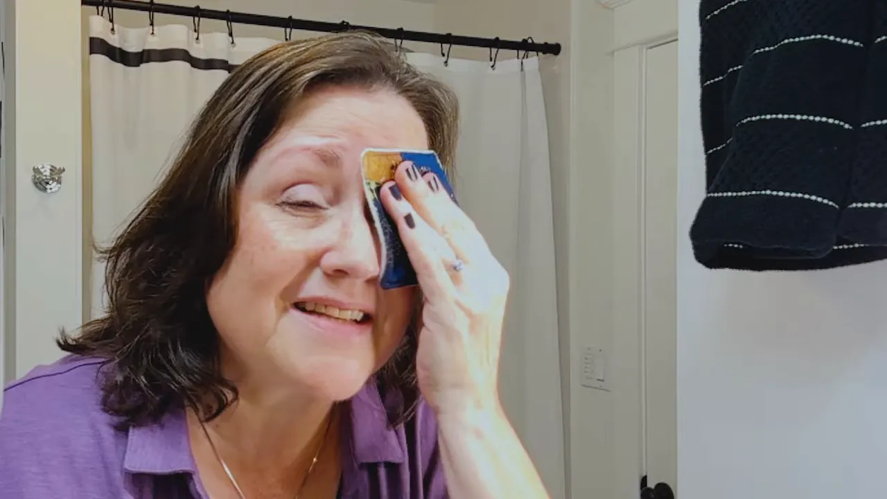 Presenter smiling while pressing a small fabric makeup pad to her eye to demonstrate removal and softness.