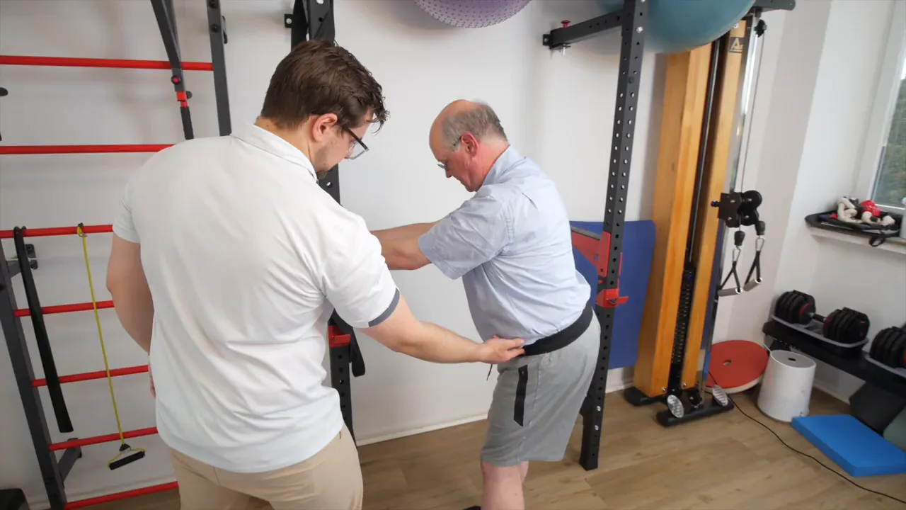 Therapeut korrigiert die Beckenstellung des Patienten durch Handkontakt am unteren Rücken