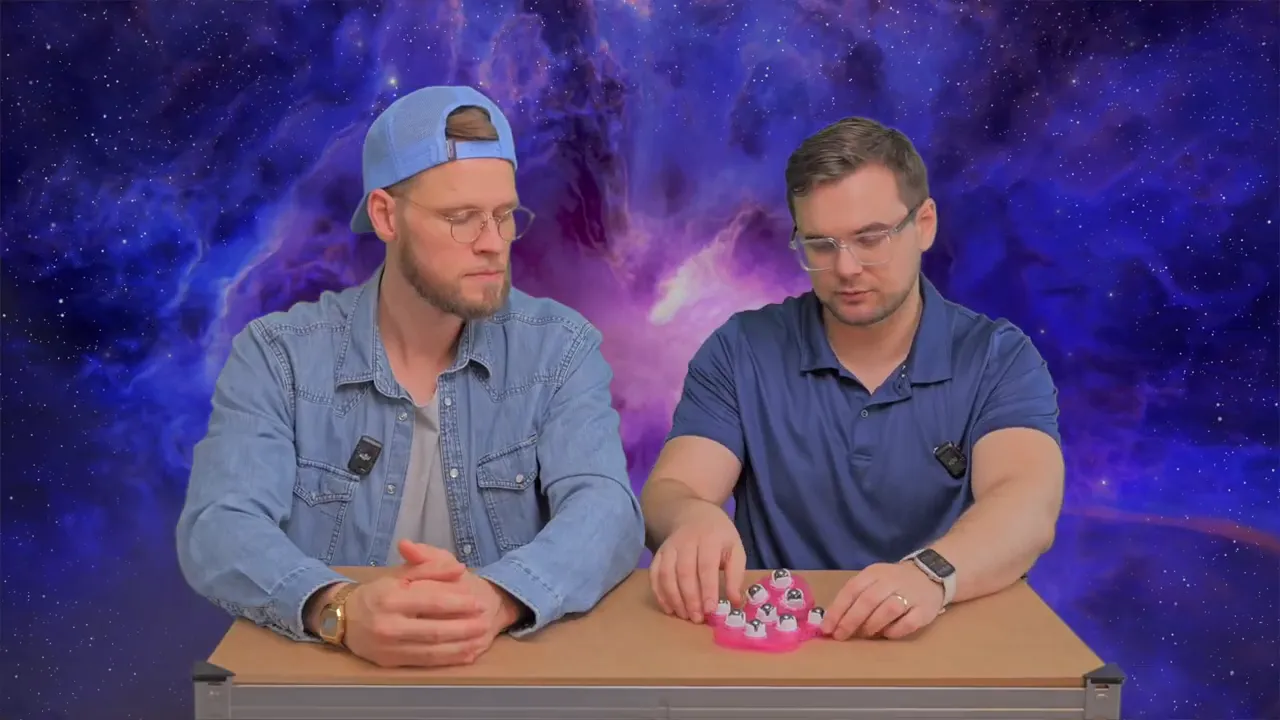 Zwei Moderatoren besprechen das Produkt, der pinke Massagehandschuh liegt deutlich sichtbar auf dem Tisch