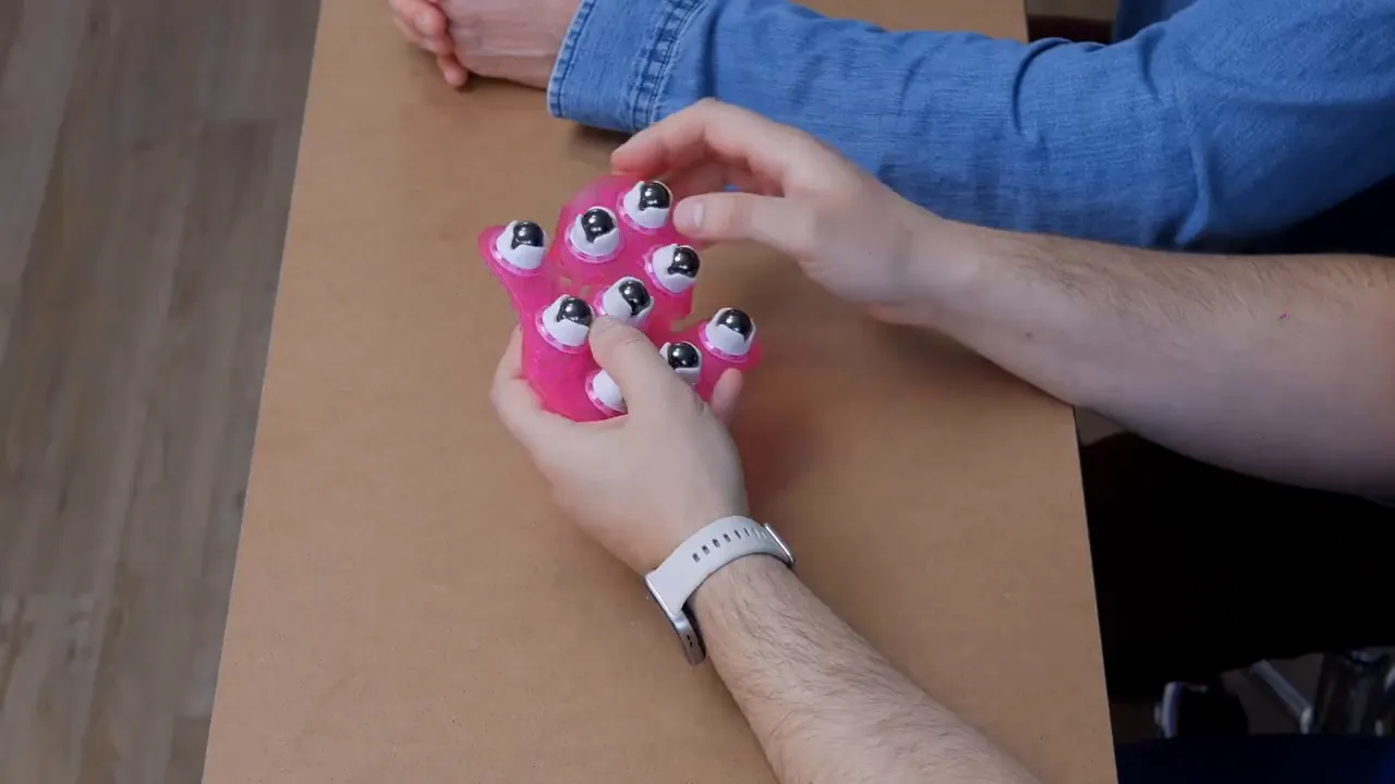 Nahaufnahme des pinken Massagehandschuhs mit sichtbaren drehbaren Kugeln, gehalten von zwei Händen