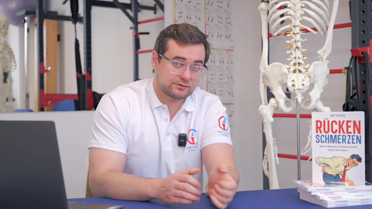 Therapeut am Tisch mit Skelettmodell und Buch 'Rückenschmerzen', erklärt Funktion statt nur Bildgebung