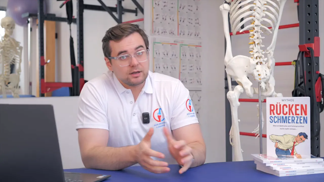 Physiotherapeut erklärt den Hüft‑ISG‑Zusammenhang neben einem anatomischen Skelettmodell und dem Buch 'Rückenschmerzen'