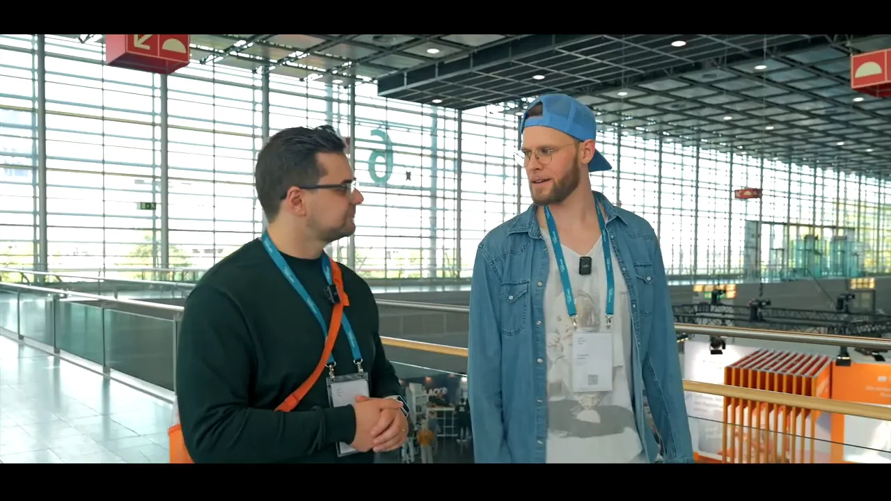 Zwei Männer diskutieren auf einer Galerie mit Blick auf Messestände im Hintergrund