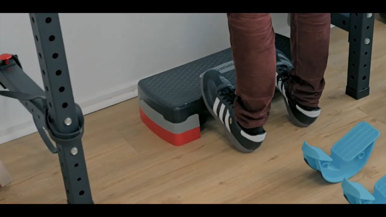 Fersen auf einer stabilen Step-Platform; blaue Kunststoff-Wadendehner liegen rechts auf dem Boden