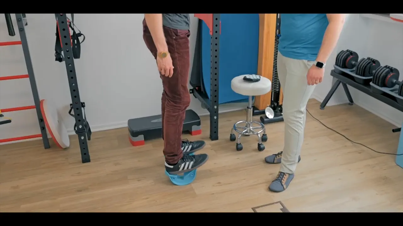 Patient steht auf kleinem blauen Wadendehner, Therapeut beobachtet aus kurzer Distanz