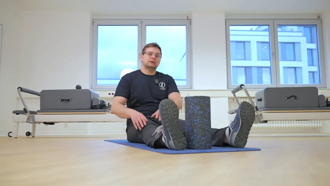 Startposition Langsitz mit Schaumstoffrolle zwischen gestreckten Beinen, Therapeut bereit zur Demonstration
