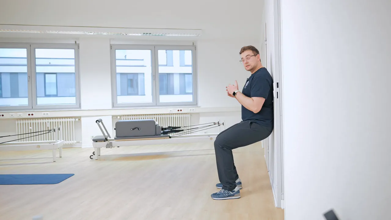 Person demonstriert Wandsitz in einer Praxis, Knie- und Hüftwinkel sichtbar