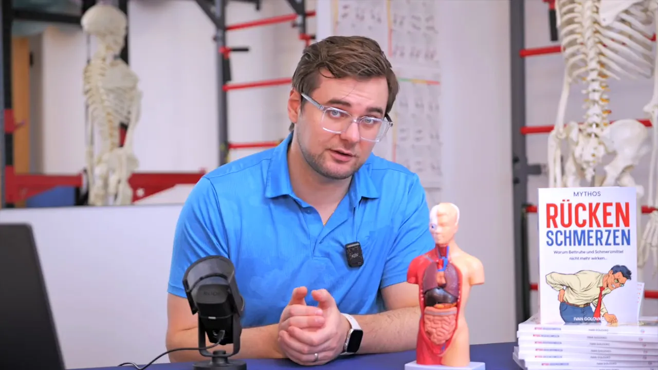 Therapeut erklärt vor einem anatomischen Torso-Modell und dem Buch 'Rückenschmerzen', klare Aufnahme.