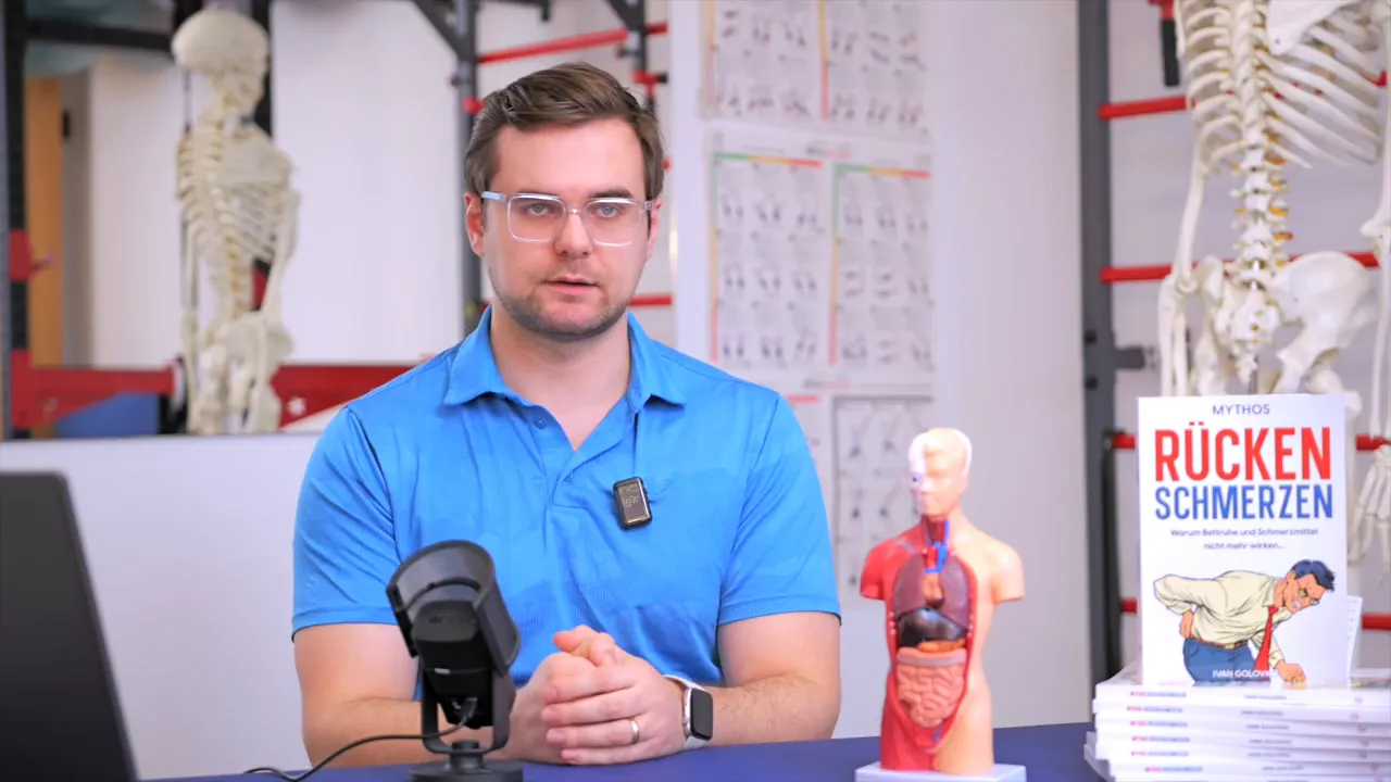 Physiotherapeut im Behandlungsraum, gut ausgeleuchtet, mit anatomischem Torso‑Modell, Mikrofon und dem Buch 'Rücken Schmerzen' sichtbar.