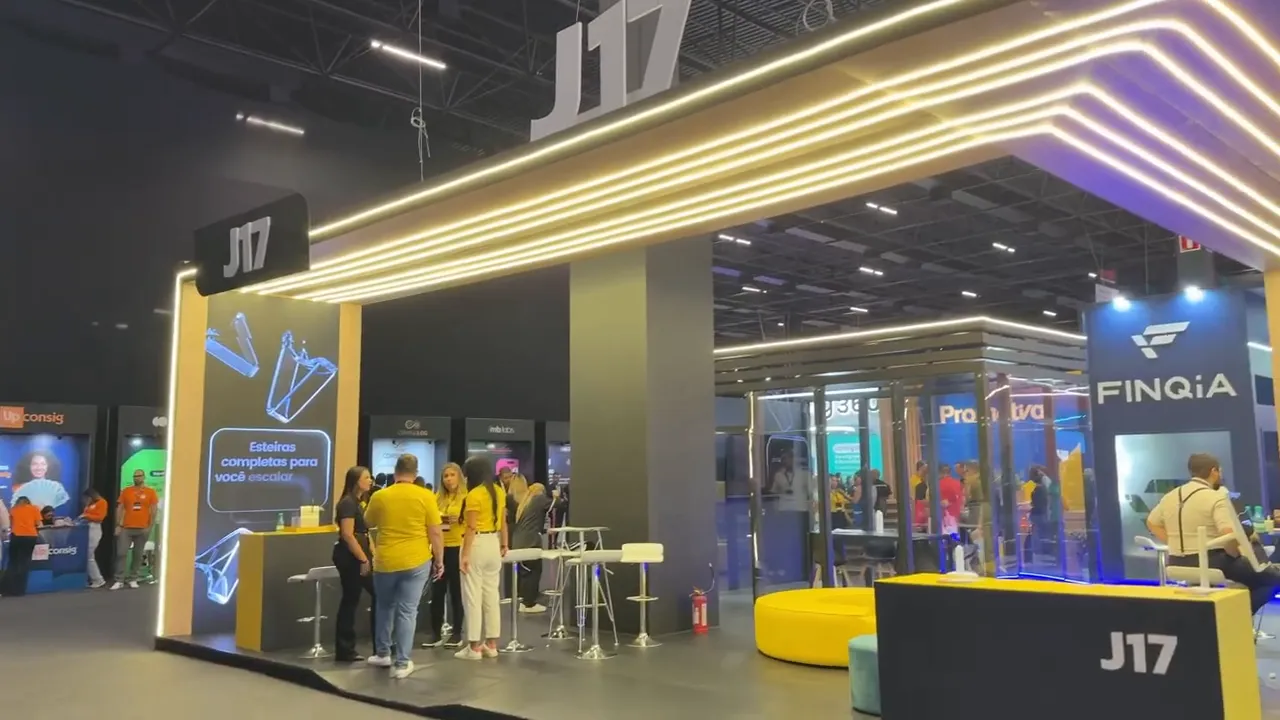Visão do estande da J17 no Corban 360 com área de atendimento e equipe circulando