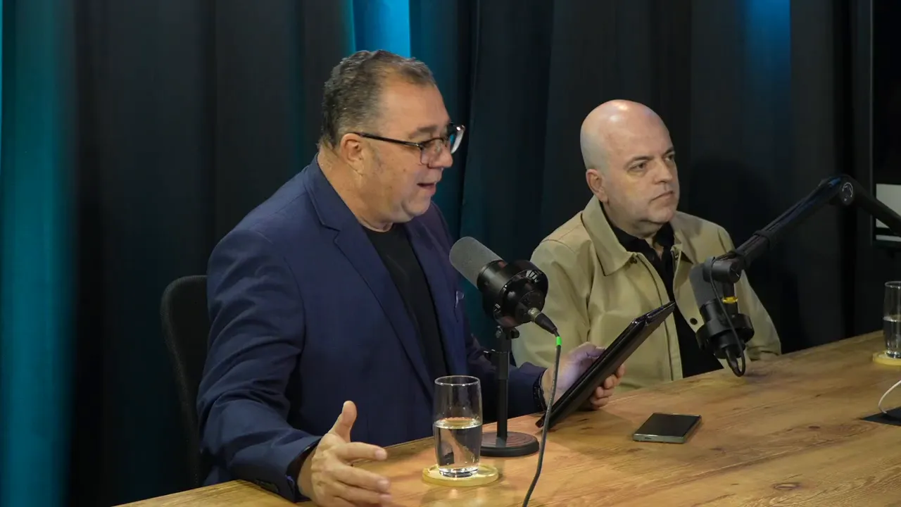 Dois convidados em estúdio de podcast; um gesticula com tablet em mãos e há microfones na mesa