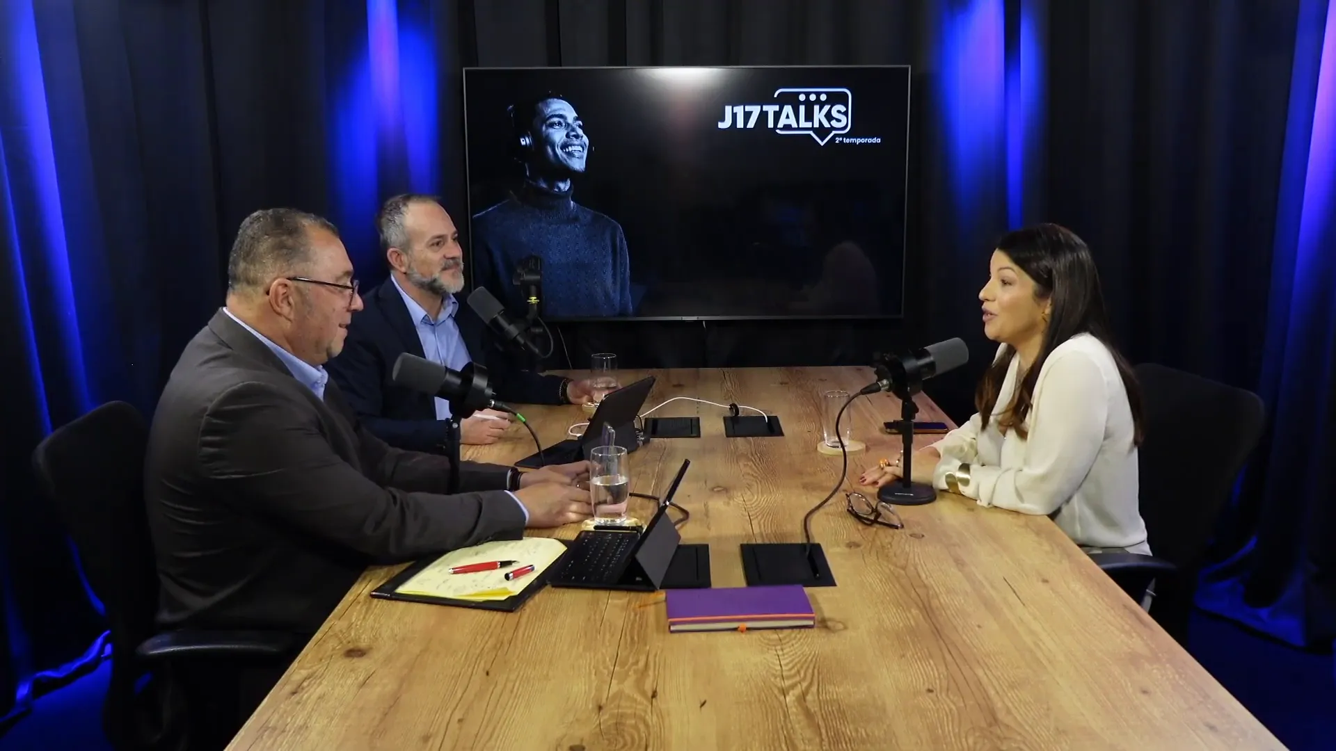 Mesa de gravação com três participantes, microfones e tela com o logo J17TALKS ao fundo