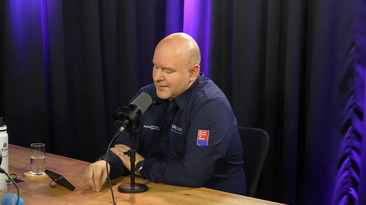 pessoa falando em estúdio de podcast com microfone, mãos sobre a mesa e aparelho sobre a mesa