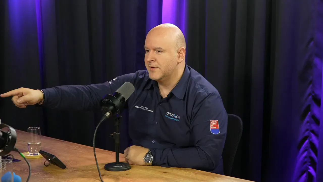 palestrante em estúdio apontando com a mão enquanto fala ao microfone, gesto indicando direção ou foco