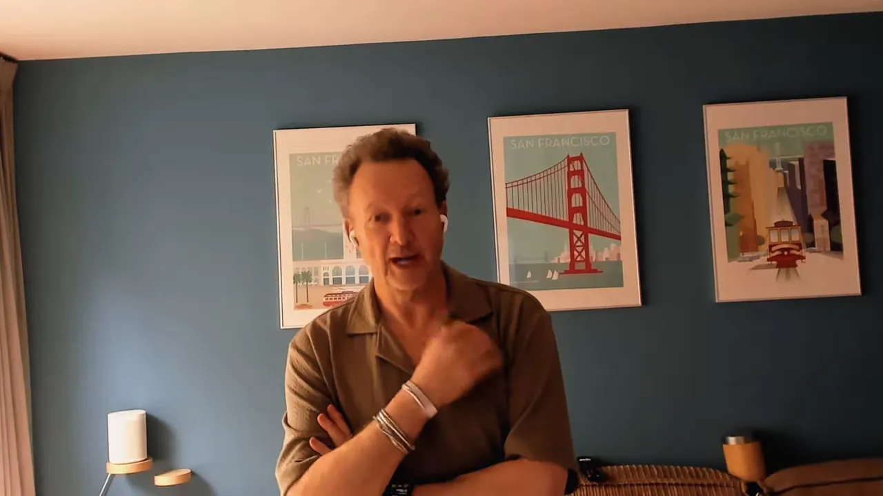 Bradley Charbonneau speaking and gesturing while seated in a studio room
