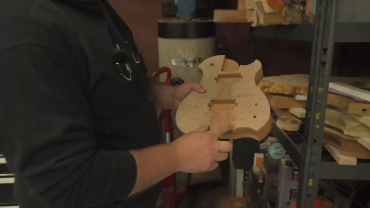Builder holding a guitar body blank with routing and template markings in the workshop
