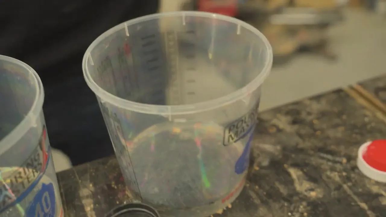 Close-up of a plastic mixing cup holding prepared material on a guitar workbench