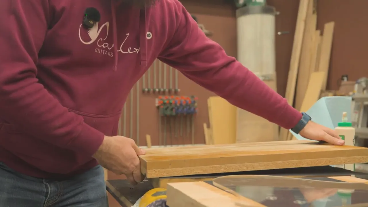 Builder using a clamp and sanding/finishing tools on a guitar body wood piece in the workshop