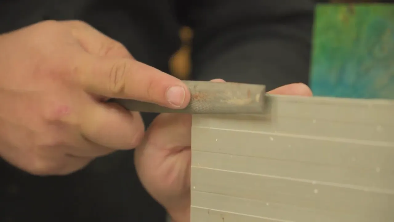 Close-up of a hand using a file to correct a bandsaw fence while wood is staged nearby