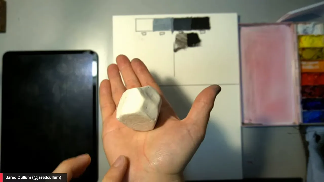 Small faceted white clay model held in hands under overhead light