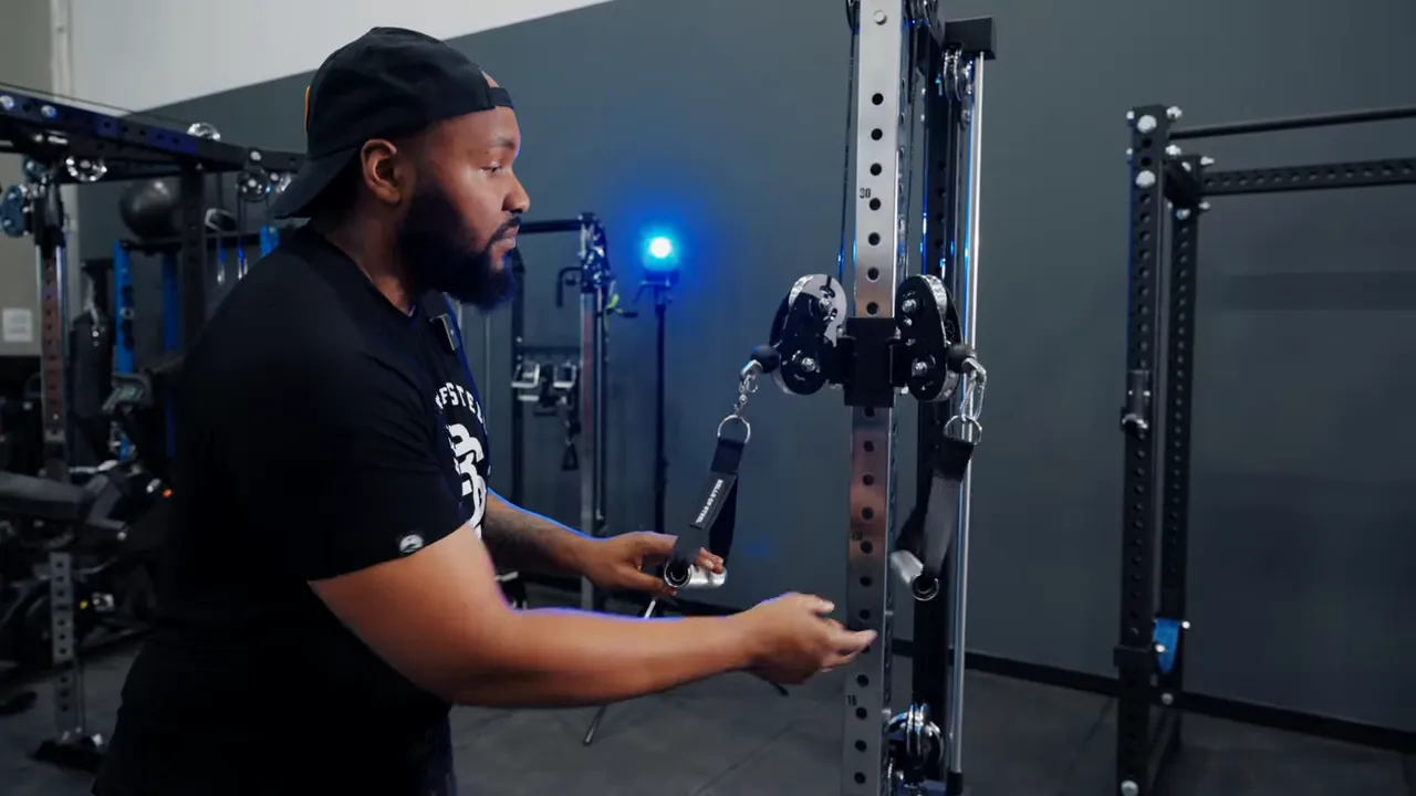 Close view of swivel shackle and fixed carabiner on a cable machine while demonstrator holds both attachments